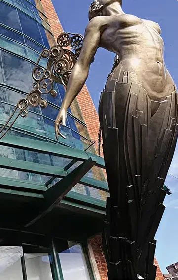 Escultura de una figura femenina con elementos mecánicos, ubicada en el exterior de un edificio en Kendall Res